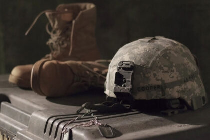 Um capacete, umas botas e umas chapas de identificação militares sobre a mala de uma arma para simbolizar a guerra no plano digital
